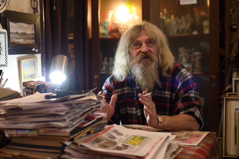 Starý muž, vetešník, v kostkované košili, s dlouhými šedivými vlasy a vousy sedí obklopený chaosem vetešnictví, čte staré noviny a kouří cigaretu. Prostor osvěcují dvě lampičky.