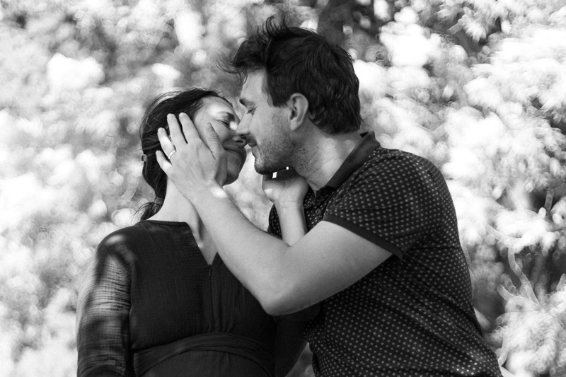 Mladý pár. On ji pladí po tváři, ona má zavřené oči a téměř se dotýkají rty. Je v tom hluboký cit. Černobílá fotografie.