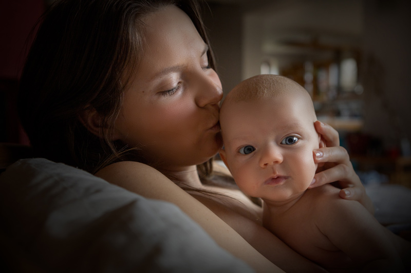 Pladá maminka se mazlí s dvouměsíčním miminkem. Skin to skin. Líbá ho na hlavičku.