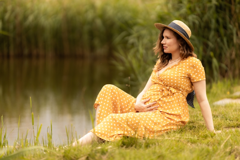 Těhotná maminka sedí na břehu rybníka. Hladí si břicho.