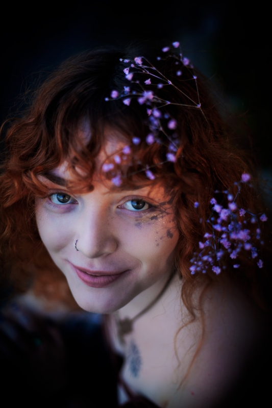 Krásná dvacetiletá rusovlasá dívka se dívá nahoru, ve vlasech má fialové kvítky nevěstina závoje. Neobvyklý úhel záběru shora.
